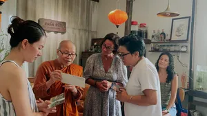 Tamu bersama tuan rumah dan seorang biksu membaca kartu bagan kelahiran Vietnam di Chan Dat Living Room, Hoi An