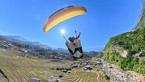 Paraglider gliding above layered terraced hills and a winding road through the valley, guided by Sapa Paragliding in Sapa, Vietnam