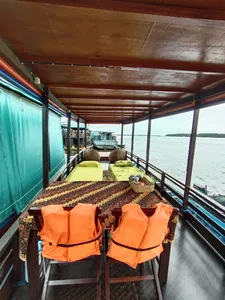 Wooden small-boat deck with bright orange life jackets and cushioned berths beside the water on a cruise in Tanjung Puting