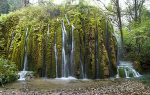 Multi-tier waterfalls in Shangri-La tumbling through a green forest, with moss-covered cliffs and misty water