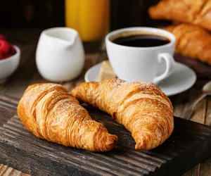 Croissant bermentega di atas papan kayu dengan secawan kopi hitam di latar semasa sesi Bake Croissants + Coffee di Singapura