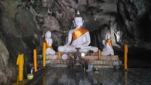 Buddha shrine altar with three seated statues and candles in a rocky cave on a Khao Sok ex-poacher trek in Khao Sok National Park