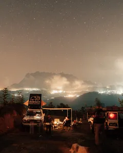 Starry night wild camping with a campfire and vans at a ridge, looking towards Mt Kinabalu from Kota Kinabalu