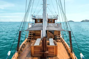 Private 3D2N Komodo cruise on a sleek white phinisi: view down the wooden bow deck with sails and sea in Labuan Bajo