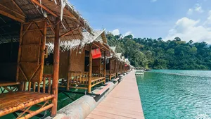 Family-run Khao Sok Riverside Cottages rafthouse walkway over the water, lined with cottages and greenery, in Cheow Lan Lake