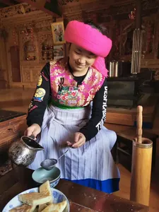 Woman in a pink headscarf preparing food at a hearth in a Tibetan home kitchen in Shangri-La during a host-led lunch