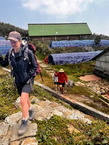 Hiker walking along a stone path past blue tarps and a green-roof shelter in Sapa on the Fansipan eco trek