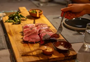 Sliced grilled beef on a wooden carving board with dipping sauces, while a hand carves and serves at private dining Singapore