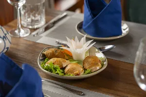 Garnished plated appetiser on a wooden dining table on a Cat Ba boutique cruise, served with utensils and tableware