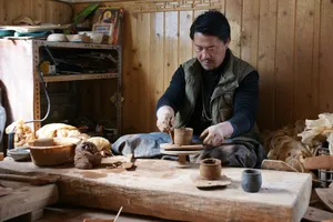 Potter at a workbench carving and shaping small cups from clay in a Shangri-La Tibetan home workshop during pottery time
