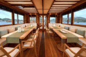 Spacious phinisi lounge with bench seating and long tables, set above the waves on a Komodo Island shared trip