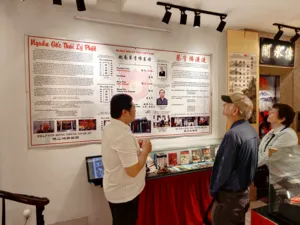 People browse boards and books at a martial arts exhibition, with Vietnamese and Chinese text posters on the walls in Ho Chi Minh City