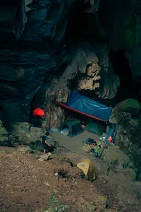Campsite inside Phong Nha-Kẻ Bàng cave with tents and travellers resting on rough ground on a Greenland Tours trip