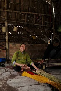 Traditional craft stall in Hoi An at dawn, with a smiling worker arranging yellow straw bundles in a rustic workshop