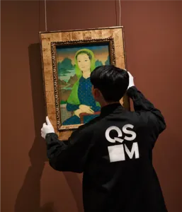 A guide from Quang San Art Museum adjusts a framed Vietnamese portrait for visitors during an art tour in Ho Chi Minh City