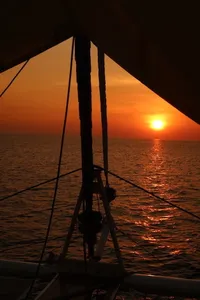 Siluet layar dan tali-temali berlatar matahari terbenam di laut semasa pelayaran yacht persendirian waktu senja dari Kota Kinabalu, Sabah