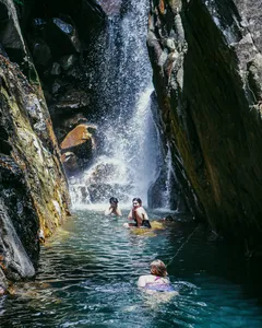 People wading in a narrow gorge pool as water cascades down the rocks on a Hoi An secret waterfall stop