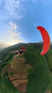 Paragliding over Sapa terraced valleys at sunset, red canopy overhead as a tandem rider floats above farmland