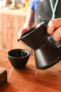 Hand-pouring dark coffee from a metal jug into a small cup during a specialty Yunnan coffee tasting in Lijiang