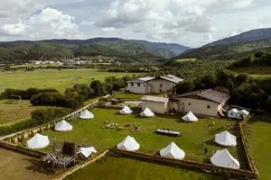 Aerial view of a Tibetan mountain valley camp at Ferme Liotard in Shangri-La with white tents, paths and surrounding hills