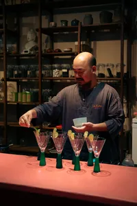 调酒师在会安品鉴站为客人倒出绿色瓶中的酒，桌上摆有鸡尾酒杯和装饰配料