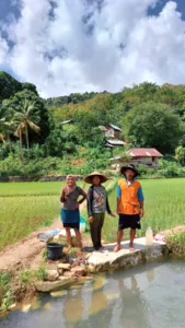 Tiga pengembara berdiri di tepi saluran air kecil di tengah kehijauan bakau yang rimbun dan rumah-rumah berhampiran Labuan Bajo