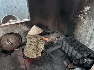Conical-hatted cook tending a smoky stove in a Hanoi home kitchen, where tofu is prepared traditionally