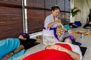 Practitioner holding wooden chimes beside a guest lying on a mat, with brass singing bowls set out for sound healing in Canggu