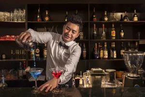 Oasis Bay Party Cruiser bartender shaking and pouring cocktails behind a bar of bottles on a Halong Bay cruise