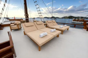Komodo Island phinisi upper deck laid out with cushioned sun loungers and folded towels, framed by sail spars and sea views