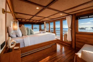 Cozy phinisi cabin with a made bed, throw pillows and ocean-facing windows, set for relaxed 3D2N shared Komodo Island