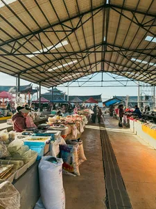Long covered village market lane with stall tables of packaged goods and fruit, during a guesthouse stay trek in Lijiang, Yunnan