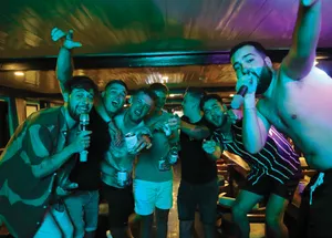 Group of friends cheering and drinking on board Oasis Bay Party Cruise at night under neon lighting, with drinks in hand in Halong Bay