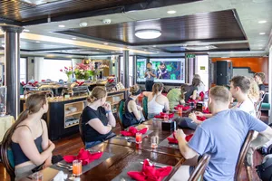 Social dining on the Oasis Bay Party Cruiser, with travellers seated at set tables inside the dining deck on a cruise in Halong Bay