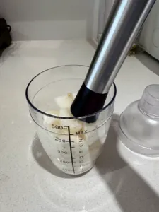 Metal blending tube over a litre-measuring beaker of pale mixture, suggesting TCM mocktail base preparation—workshops in Singapore