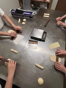 Baker hands pressing and folding shio pan dough shapes on baking paper beside tools during workshops in Singapore