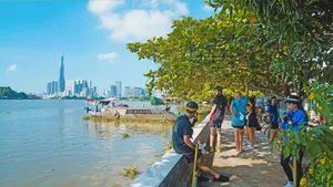 People walking along a quiet riverbank path on Mekong Island, with Ho Chi Minh City skyline across the water
