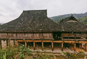 Rumah kayu tradisional beratap sirap gelap di Xishuangbanna, berada di tengah taman yang rimbun dalam perjalanan pribadi sehari