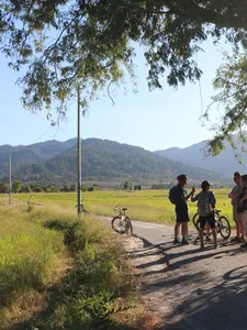 Cyclists on a countryside lane in Langkawi with bicycles by the roadside and mountain hills ahead during Dev's Adventure Tours