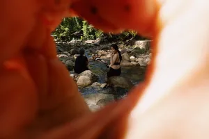 View through a circular blur shows travellers resting by a rocky stream near Langkawi riverbank on a cycling break