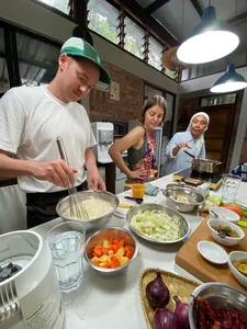 Guests chopping vegetables and stirring pans at Kebun Lidstari farmhouse kitchen in Langkawi during a Malaysian cooking session