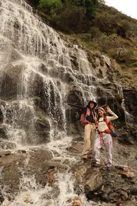 Hikers posing beside a cascading waterfall on the Tiger Leaping Gorge high trail in Lijiang, trekking poles and backpacks