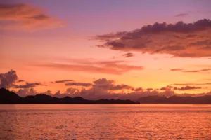 Warm golden sunset over the sea with distant island hills on the horizon, calm bay at dusk, Labuan Bajo
