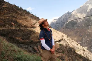 Trekker looking up at the cliffs on Tiger Leaping Gorge’s trail near Lijiang, wearing a brimmed hat and trekking poles