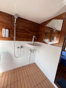 La Famille ensuite on a wooden phinisi showing a countertop sink, overhead shower rail, and mirror as the cruise sails Labuan Bajo
