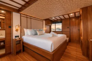 New phinisi bedroom on the deck near Labuan Bajo, with a made-up double bed, wooden walls and sea-view windows