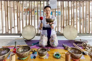 ADDA Yoga sound healer seated with singing bowls on a rooftop mat in Canggu, Bali for a sound healing session