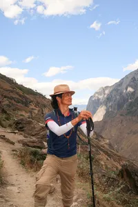 Trekker on a mountain path with trekking poles overlooking Tiger Leaping Gorge in Lijiang, wearing a wide-brim hat