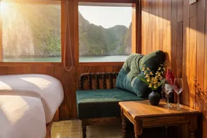 Cosy wooden cabin lounge on Cat Ba Ocean Cruises’ 3D2N Cat Ba boutique cruise, with sofa, wine glasses and sea-view window