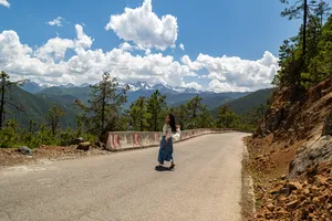 Walker on a mountain road near Shangri-La, with Meili Snow Mountain’s snowy peaks across the valley under blue sky